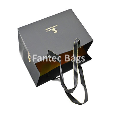 "Luxury black kraft paper shopping bag with matte finish, gold foil logo, and ribbon handles."