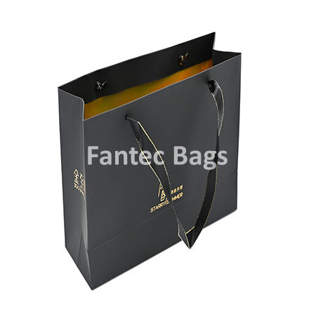 "Matte finish kraft paper shopping bag with ribbon handles and gold interior, displayed upright for retail presentation."