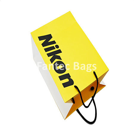 "Eco-friendly kraft paper shopping bag with yellow front, white sides, and black rope handles, shown laying flat."